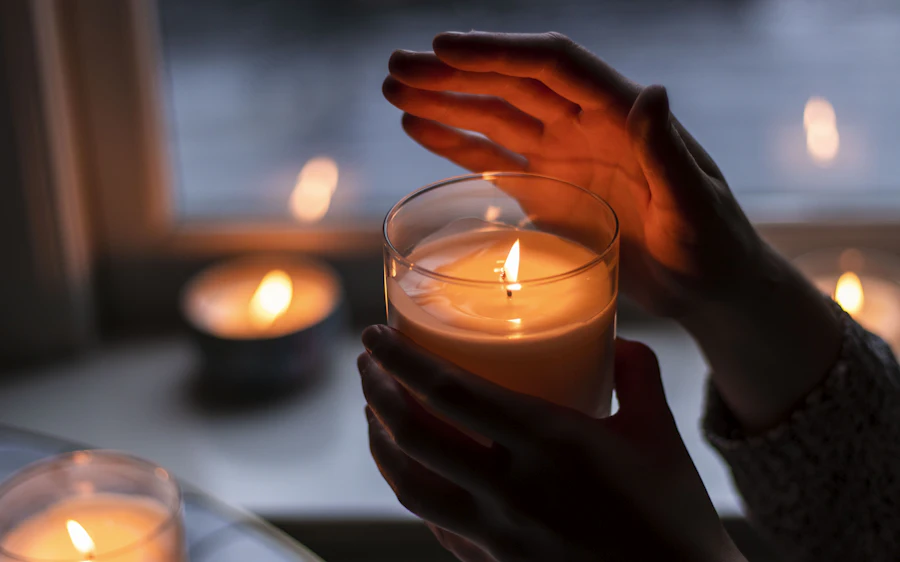 Manos sujetando una vela encendida en un vaso de cristal